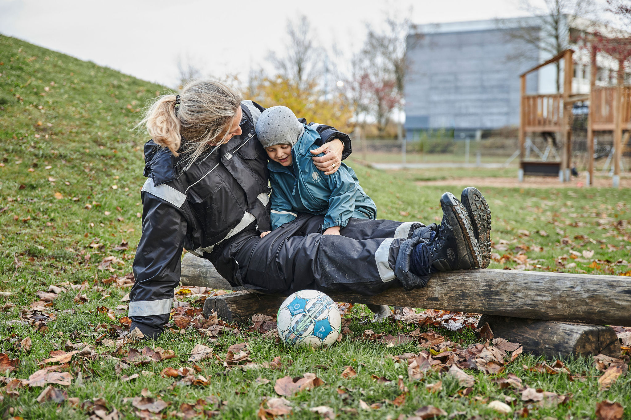 Billede af en smilende og opmærksom voksen, der sidder på jorden, mens hun holder om en dreng, som sidder på hendes ben. 